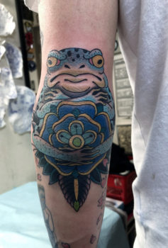 花の後ろで腕組みをするカエルが描かれたタトゥー